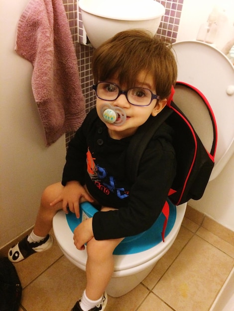 Hooghoekportret van een jongen op een toiletbak met een speen