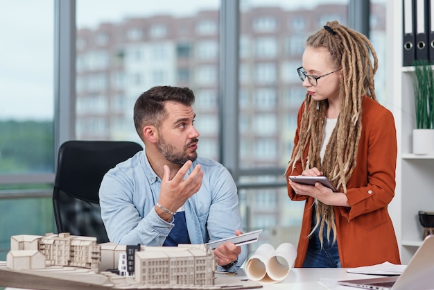 Hoogopgeleide hardwerkende creatieve mannelijke en vrouwelijke ontwerpers die werken met mock-up van toekomstige gebouwen