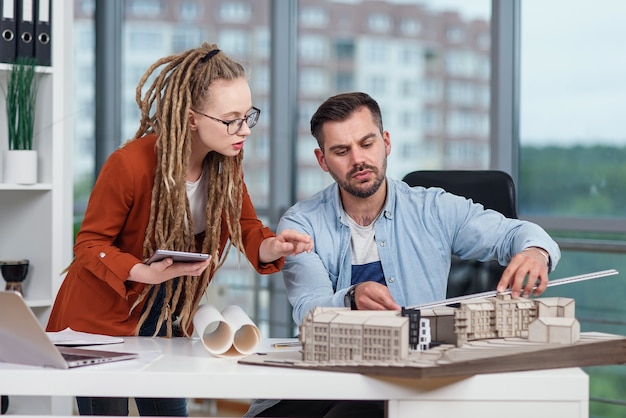 Hoogopgeleide hardwerkende creatieve mannelijke en vrouwelijke ontwerpers die werken met mock-up van toekomstige gebouwen