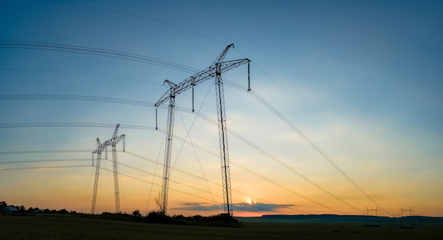 Hoogspanningstorens met elektrische hoogspanningslijnen bij zonsondergang.