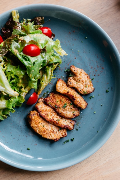 Hoogste mening van BBQ geroosterde kippenborst met salade die in blauwe plaat op houten lijst wordt gediend.