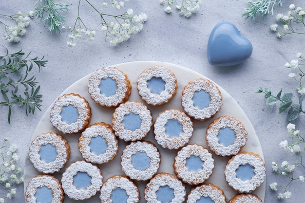 Hoogste mening van bloem Linzer-koekjes met blauwe die verglazing op lichtblauw met witte bloemen en ceramisch hart wordt verfraaid