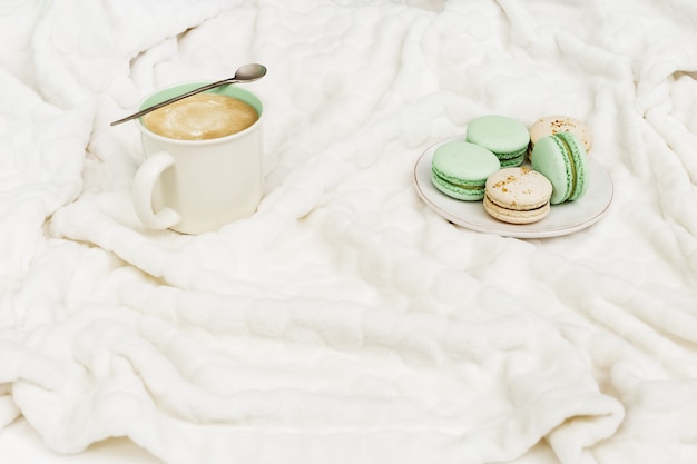 Hoogste mening van de cappuccino van de kopkoffie met smakelijke makarons op zachte witte bontoppervlakte. Warm drankje met melk en dessert. Winterochtend concept.