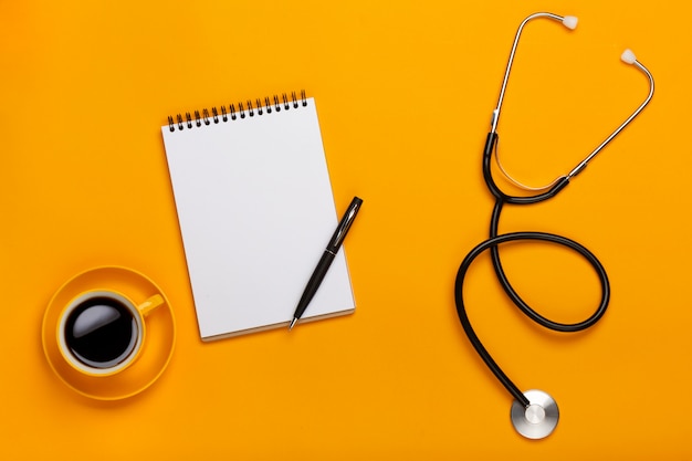 Hoogste mening van de lijst van een arts met blocnote en penstethoscoop, toetsenbord, voorschrift en pillen, een kop van koffie op een gele achtergrond
