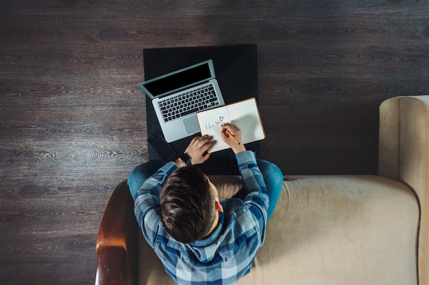 Hoogste mening van jonge freelancer die in een notitieboekje neerschrijven terwijl het werken vanuit huis