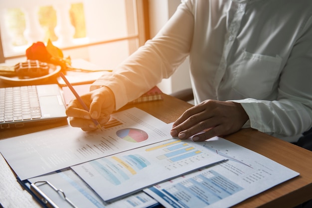 Hoogste mening van jonge werkende vrouw gebruikend laptop en lezend rapport, grafieken, grafieken, document op het werk. Bedrijfsvrouw die bij haar bureau werken.