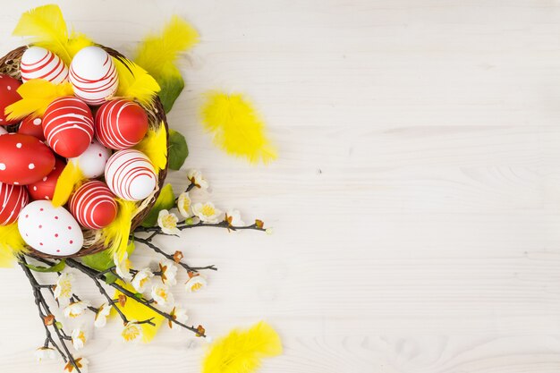 Hoogste mening van kleurrijke paaseieren in mand met gele veren en de lentebloemen op een lichte houten achtergrond met berichtruimte.