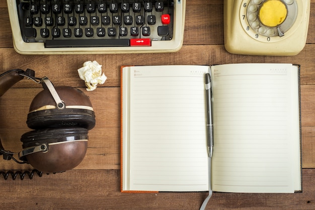 Hoogste mening van notitieboekje op de houten lijst, de schrijfmachine, de oude telefoon en de oortelefoon