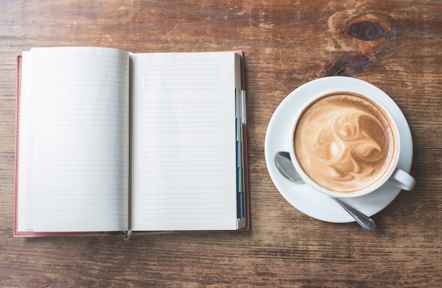 Hoogste mening van open notitieboekje met kop van koffie op houten lijst.