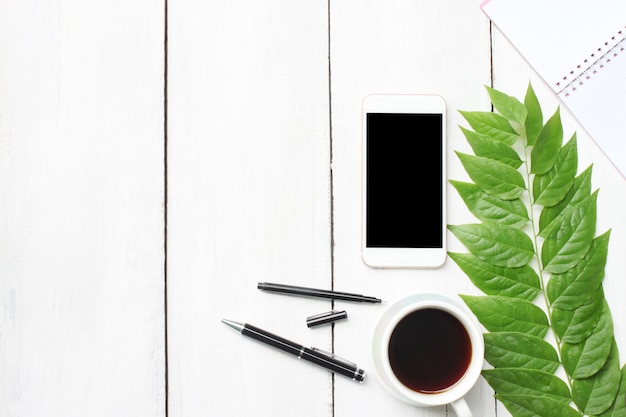 Foto hoogste mening witte houten bureaulijst met smartphonelevering en koffiekop.