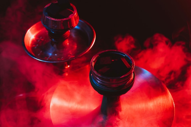 Hookah bowl, shisha and coals close-up on a smoky black background with colored lighting