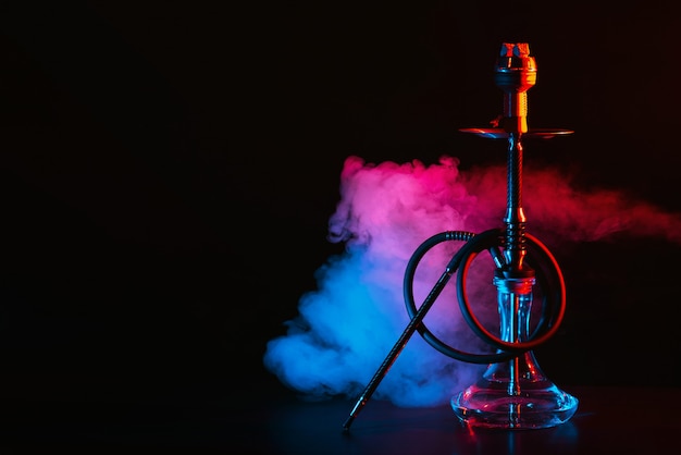 Photo hookah with a glass flask and a metal bowl shisha with colored smoke on the table