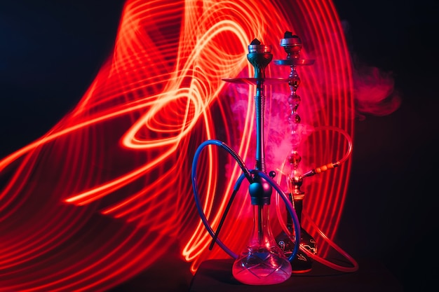 Narghilè con carbone shisha caldo con illuminazione al neon rossa e blu su sfondo scuro