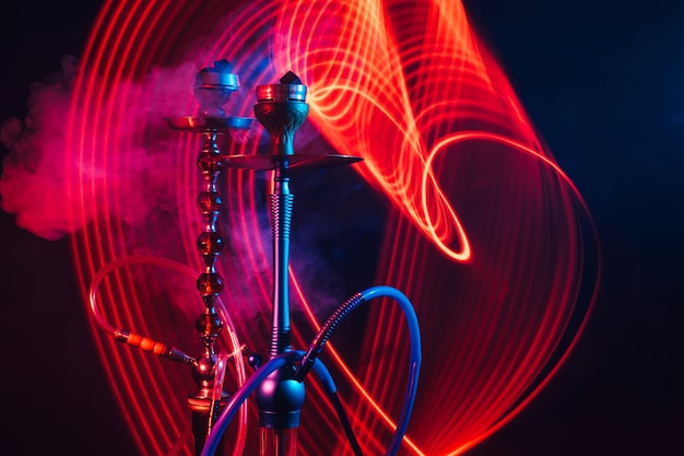 Narghilè con carbone shisha caldo con illuminazione al neon rossa e blu su sfondo scuro