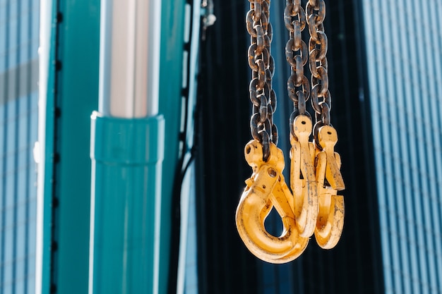 The hooks of the mobile crane near the glass of high buildings.Lots of hooks hanging from chains suspended from a crane.