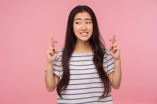 Hoop en wensen voor fortuin Portret van bezorgd meisje met lang donkerbruin haar met vingers gekruist voor goed geluk uiten van grote wens om te winnen indoor studio shot geïsoleerd op roze achtergrond