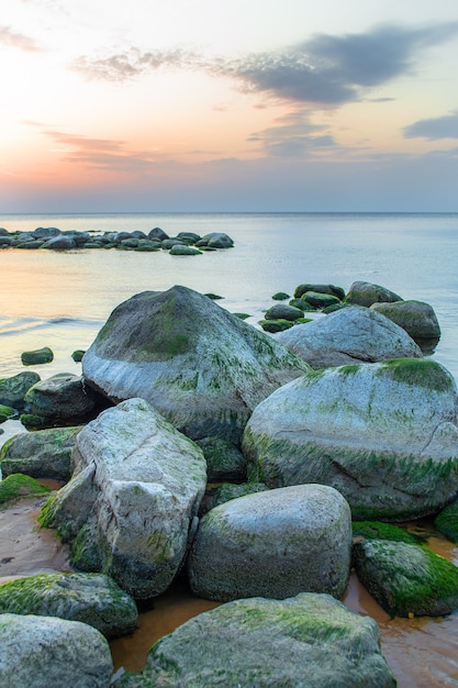 Hoop grote rotsblokken op de voorgrond en een strook kleine rotsen op de achtergrond. Rotsachtig strand