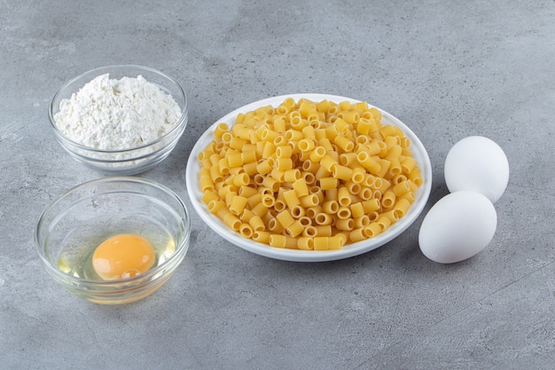 Hoop rauwe pipet rigate pasta in een witte kom met eieren en bloem.