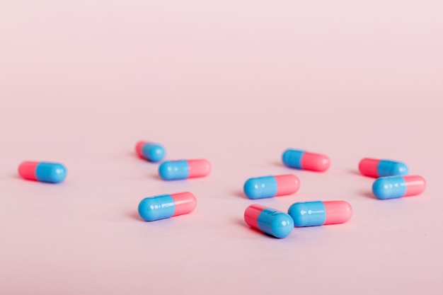 Hoop roze en blauwe pillen op gekleurde achtergrond Tabletten verspreid over een tafel Stapel rode zachte gelatinecapsule Vitaminen en voedingssupplementen concept