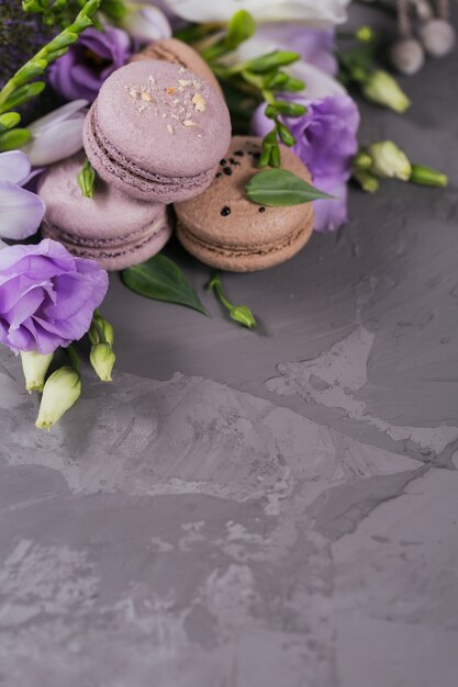 Hoop van zoete Franse macarons gemengd met bloemen op een grijze betonnen ondergrond. Pastelkleurige bitterkoekjeskoekjes. Voedsel-, culinair-, bakkerij- en kookconcept