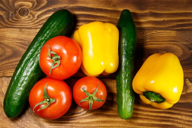 Hoop verse groenten op de keukentafel. Rijpe tomaten, paprika's en komkommers op houten achtergrond. Bovenaanzicht