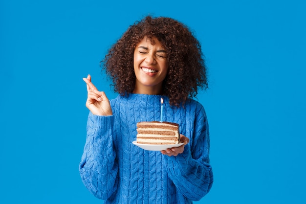 Hoopvol en opgewonden, schattige Afro-Amerikaanse vrouw in trui, wens en kruis vingers