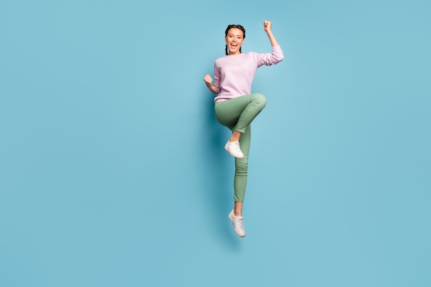 Hooray! Full body photo of funny lady jumping high good mood win sportive competition championship wear casual pink pullover green trousers shoes isolated blue color