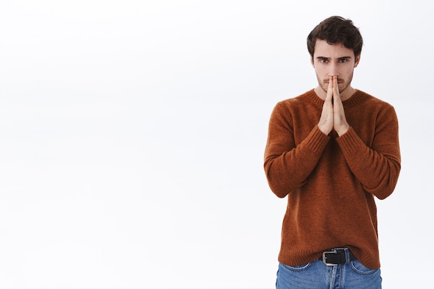 Hopeful concerned young man praying for good outcome, feel worried for friend got trouble, hold hands in pray near face