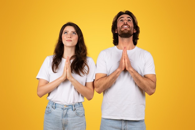 Foto una coppia speranzosa con i palmi stretti in preghiera che guarda in alto con espressioni contemplative