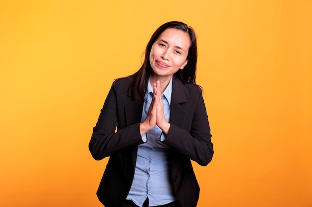 Hopeful filipino woman doing praying gesture with hands, being religious in studio over yellow background. Spiritual adult asking god for forgiveness, expressing hope and belief. Religion concept