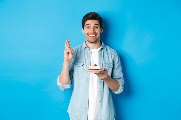 Hopeful man holding birthday cake and cross fingers