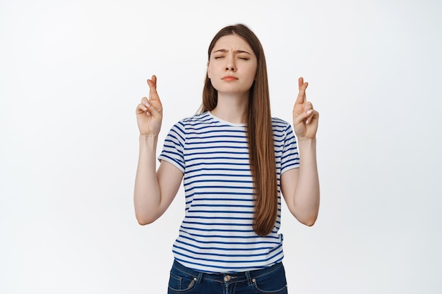 Hopeful young woman cross fingers and begging, making wish, anticipating news on white