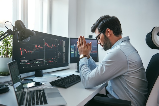 Hoping for the success side view of tired young businessman or trader holding palms together