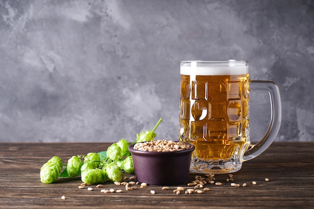 Hops and glass of light beer on wooden space, place for text.