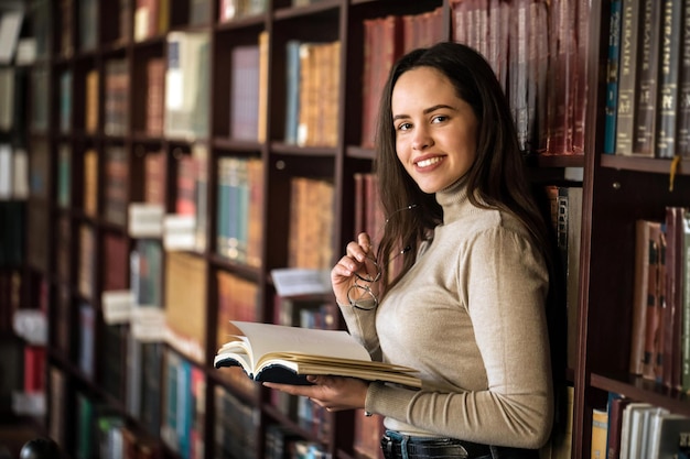 Horizontaal beeld van een donkerbruin meisje met open boek op een achtergrond van planken met boeken