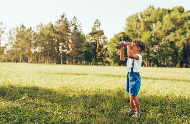 Horizontaal beeld van kleine jongen die door de verrekijker kijkt op zoek naar een verbeelding of verkenning in de zomerdag in het park Gelukkig kind speelspel buitenshuis Jeugdconcept