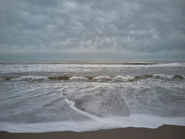 Horizontaal schot van de zee die op een bewolkte dag vanaf het strand verloren gaat aan de horizon.