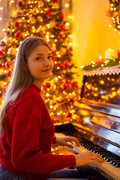 Horizontaal schot van jonge vrouwelijke pianiste die haar instrument bespeelt in de buurt van de versierde kerstboom