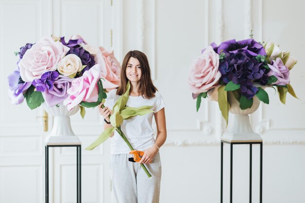 Horizontaal schot van mooie brunette jonge vrouw siert hal voor bruiloft houdt tuintang maakt boeketten van kunstbloemen houdt van ontwerpen Mensen en bloemen ontwerpen concept