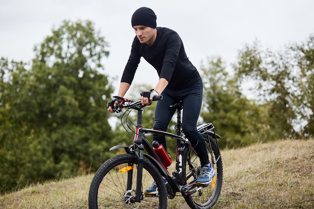 Horizontaal schot van personenvervoerfiets, bomen en blauwe hemel, aantrekkelijke kerel die zwarte sportslijtage dragen