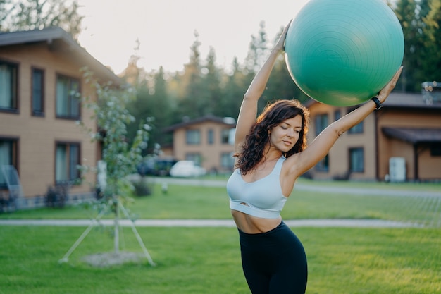 Horizontaal schot van slanke donkerbruine Kaukasische vrouw praktijken yoga met geschiktheidsbal