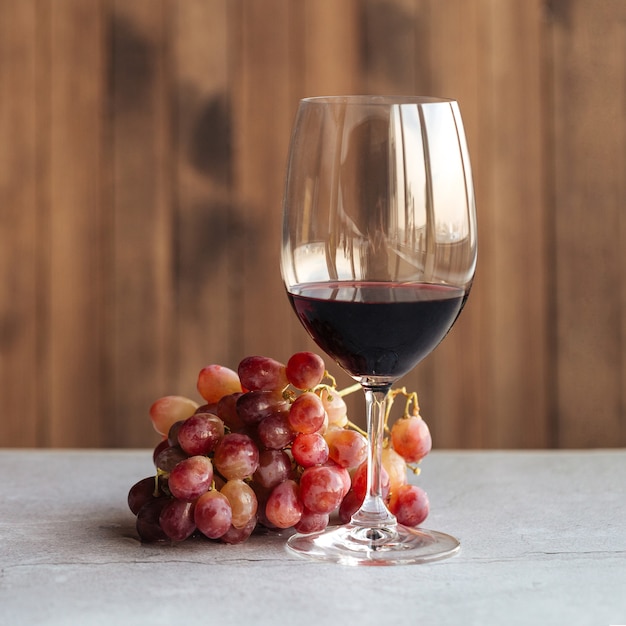 Horizontaal zijaanzicht op een glas rode wijn met druiven op tafel