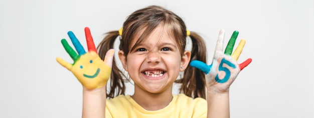 Horizontal banner or header with happy toothless little girl with the five number painted on the hand laughing and having fun Little girl painting her hands with smiley faces and numbers