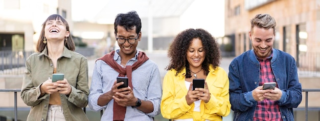 Horizontal banner or header with multiracial friends laughing using smartphone in the university district of the city Young people addicted by mobile smart phones