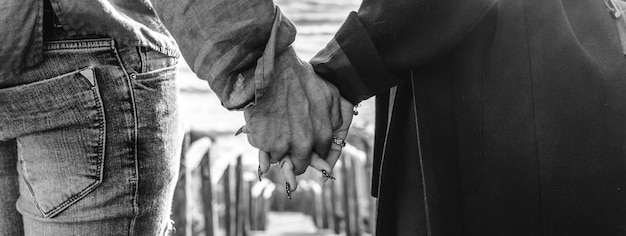 Horizontal banner with closeup of young couple holding hands walking down on wooden stair towards the beach Hipster couple holding hands in love enjoying romantic evening at beach