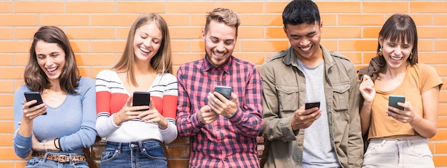 horizontal banner with multicultural friends having fun together looking at their smartphones at wall on college campus young people addicted by mobile smart phones