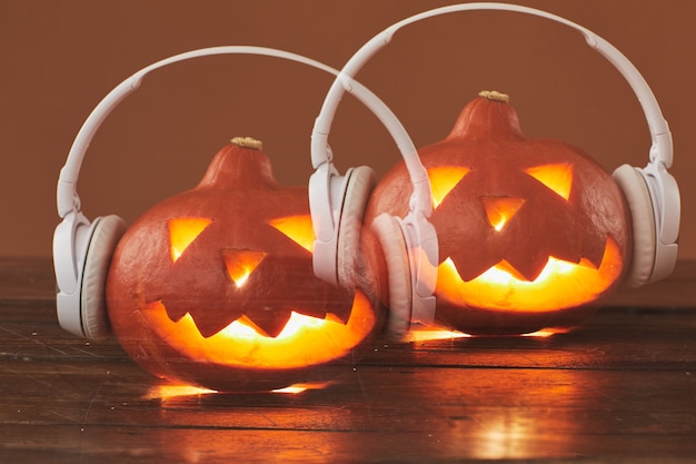 Photo horizontal close-up multiple exposition studio shot of jack o' lantern wearing white headphones against brown surface