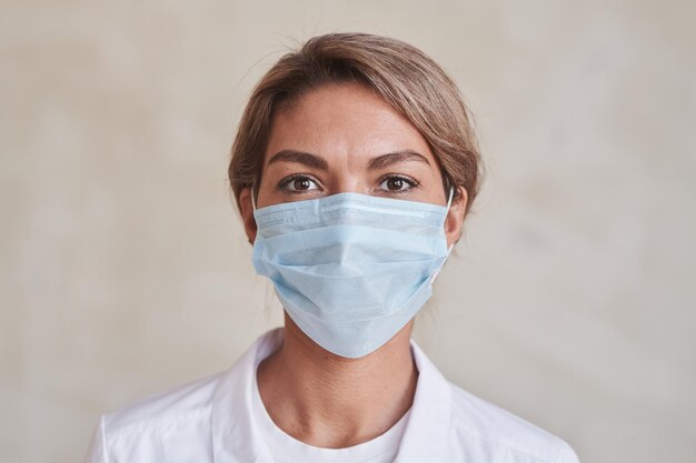 Horizontal closeup portrait of modern young adult female doctor wearing protective mask looking at c