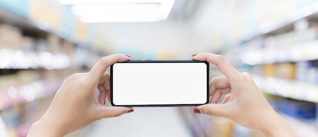 Horizontal closeup shot of female hand holding smartphone blank screen background as many shelves