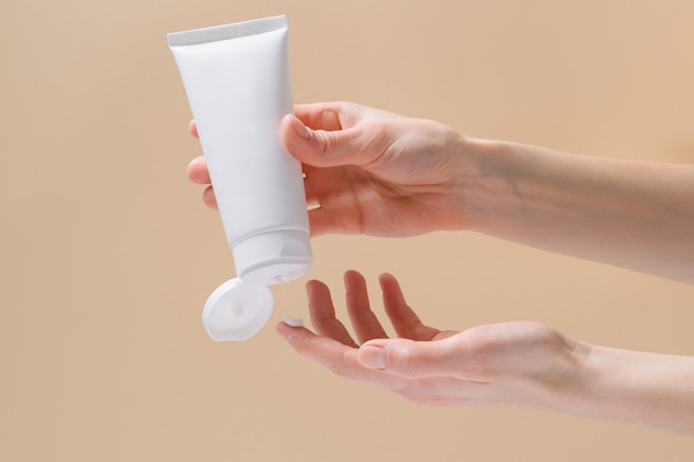 Horizontal image of female hands squeezing cream from a white blank tube Concept of cosmetology and natural skin care product Mockup for your design